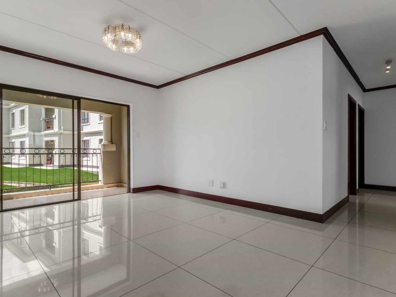 A bright, empty living room featuring polished tiled floors, dark wood-finish skirting, and a sliding glass door leading to a balcony.