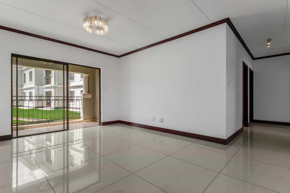 A bright, empty living room featuring polished tiled floors, dark wood-finish skirting, and a sliding glass door leading to a balcony.