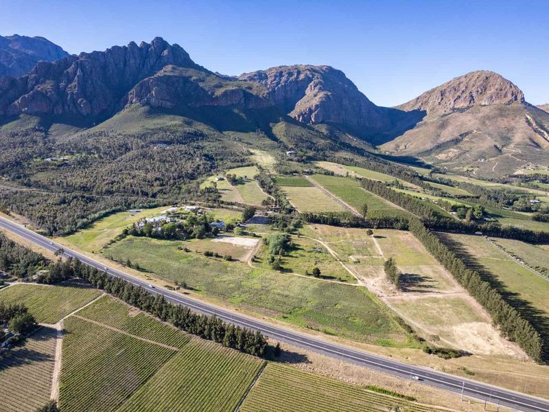 An expansive aerial view of a large farm property featuring extensive vineyards, open fields, and a scenic mountain backdrop.