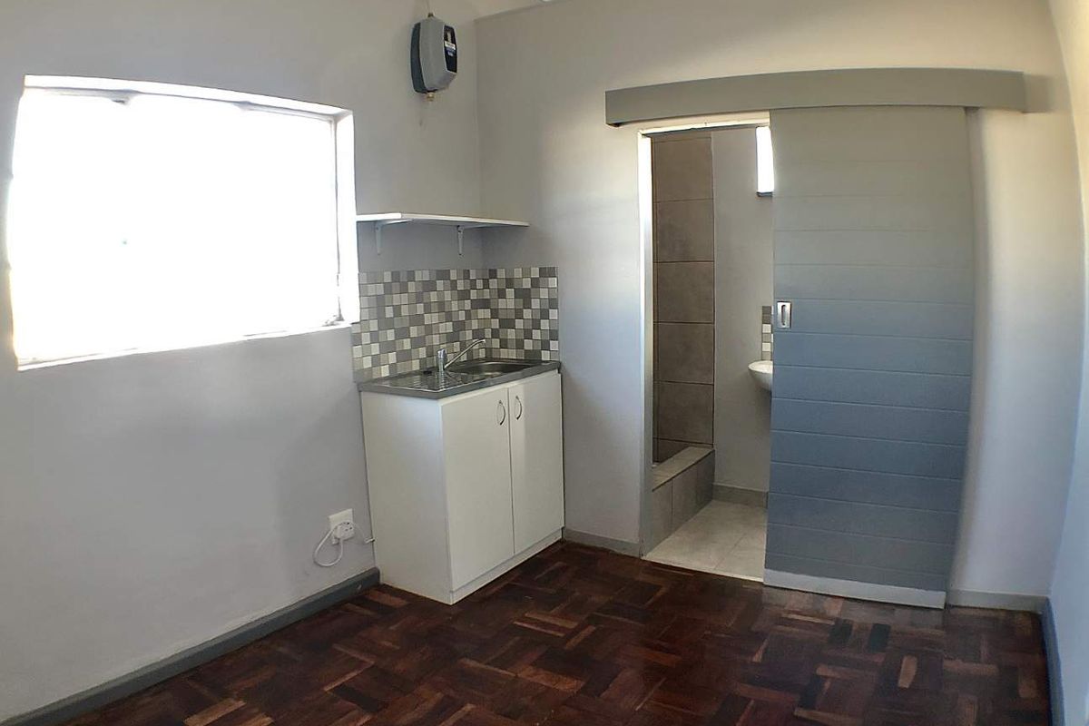 Compact kitchen area featuring parquet flooring, a small sink unit with tiled backsplash, and a sliding door leading to an adjacent bathroom.