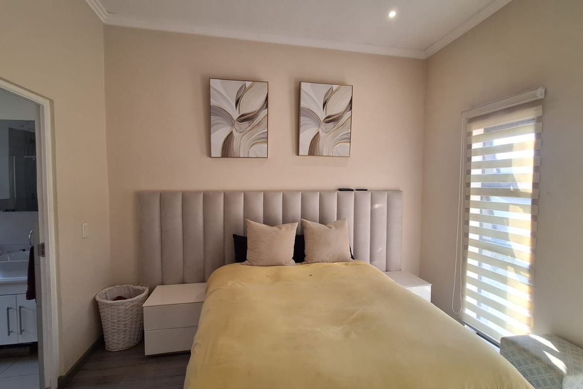 A well-maintained bedroom featuring a modern upholstered headboard, neutral wall tones, roller blinds, and direct access to an en-suite bathroom.