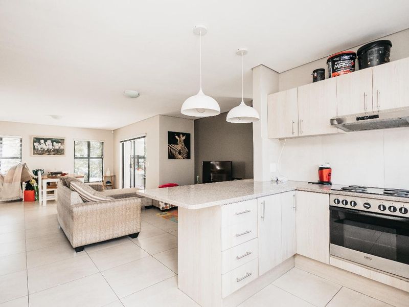 Open-plan living area featuring a modern kitchen with granite countertops, built-in oven, hob, and tiled flooring, seamlessly flowing into the adjacent living space.