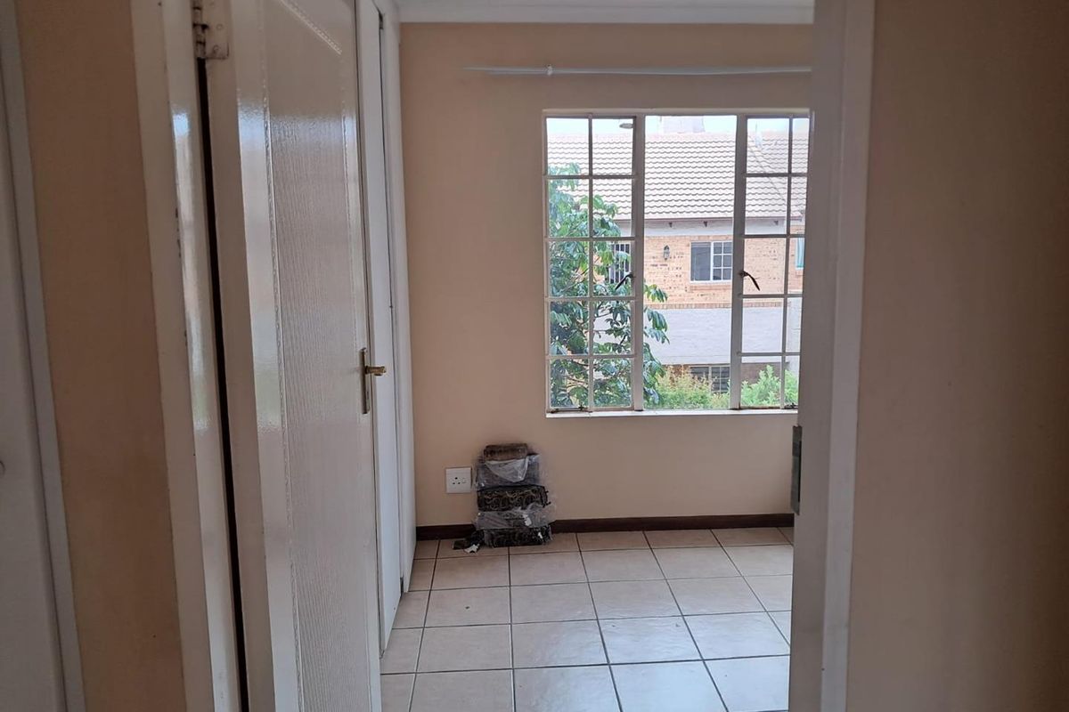 A view into an empty bedroom featuring tiled flooring, a large window with security bars, and neutral wall paint.