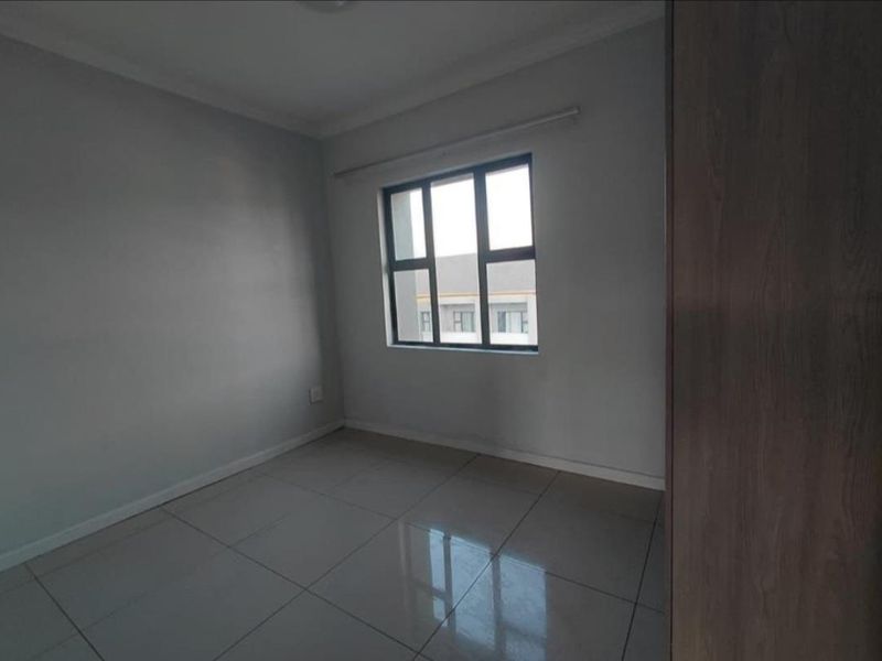 A clean, empty bedroom featuring neutral tiled flooring, grey walls, and a built-in cupboard, offering a blank canvas for personalization.