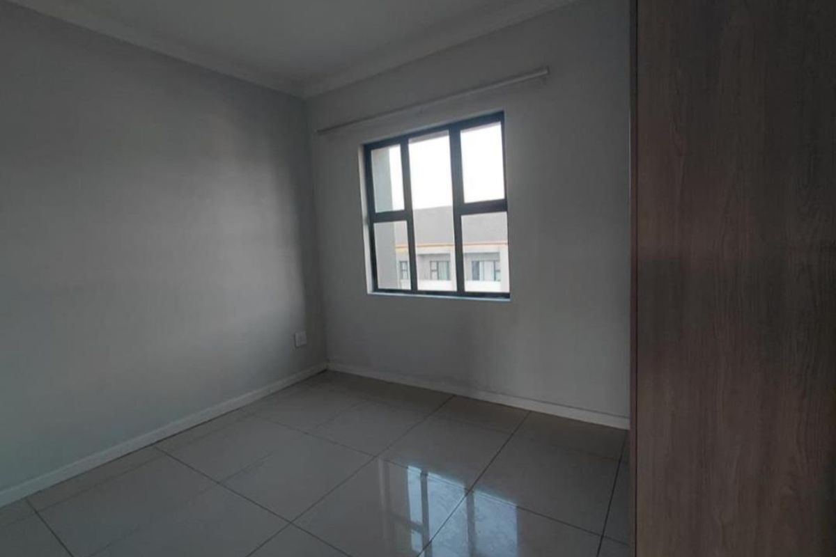 A clean, empty bedroom featuring neutral tiled flooring, grey walls, and a built-in cupboard, offering a blank canvas for personalization.