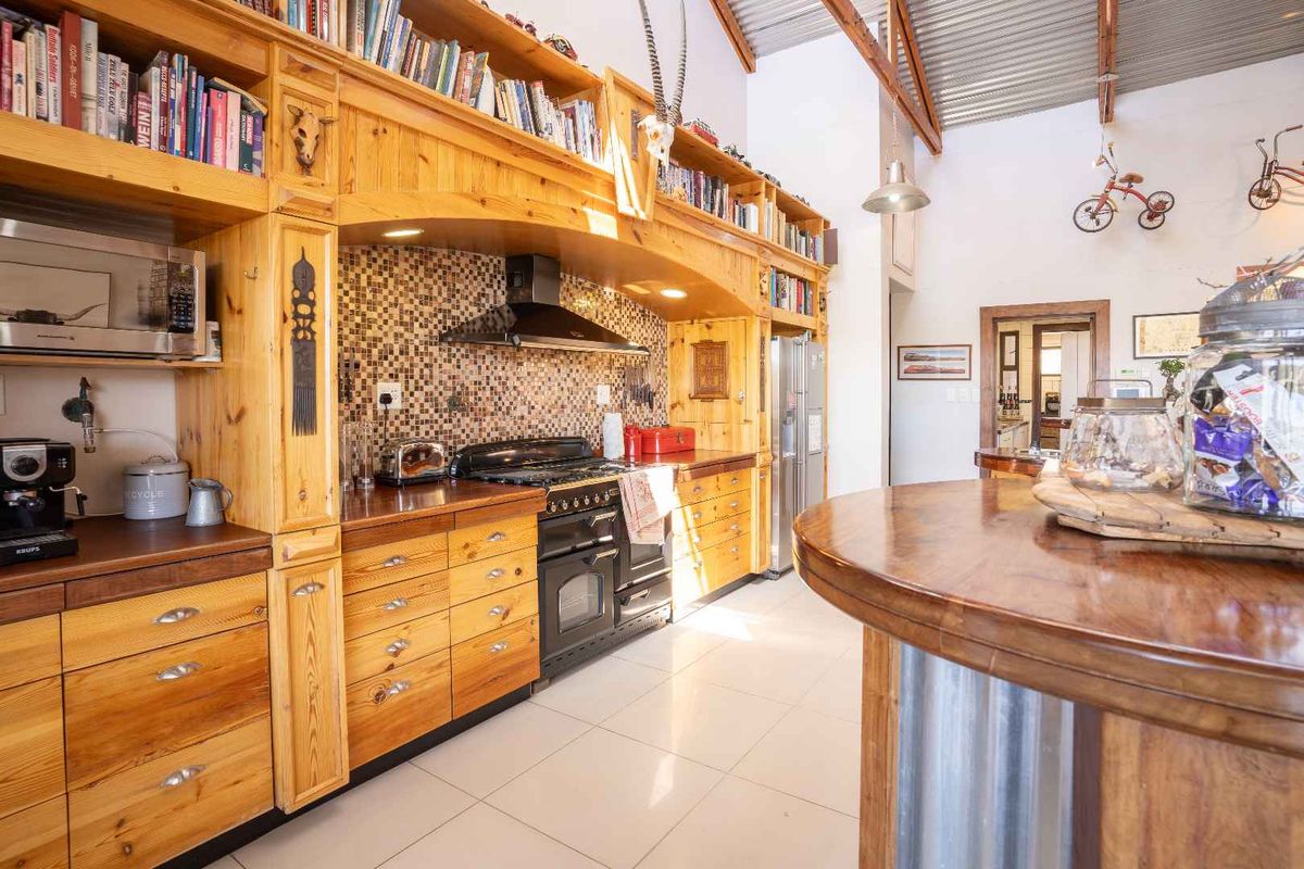 A rustic-style kitchen featuring extensive timber cabinetry, a mosaic tile backsplash, a black range cooker with extractor fan, and high vaulted ceilings.