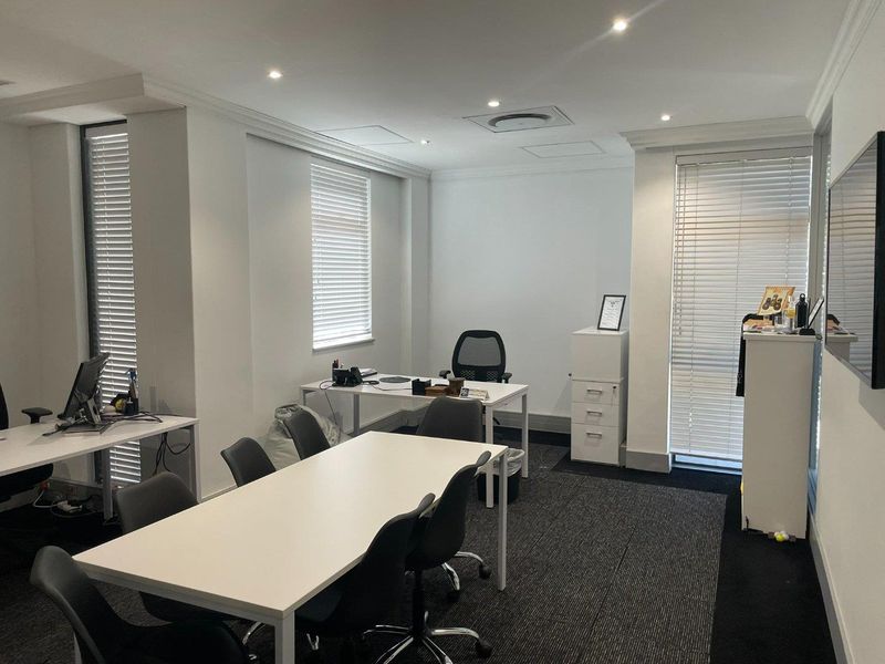 A professional office space featuring neutral walls, carpeted flooring, recessed lighting, and large windows fitted with venetian blinds.