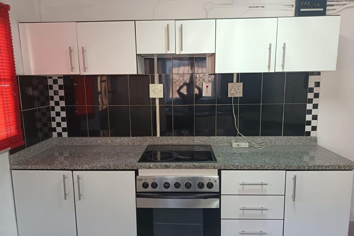 A functional kitchen featuring white cabinetry, granite countertops, a built-in electric stove and oven, and a contrasting black tiled backsplash.