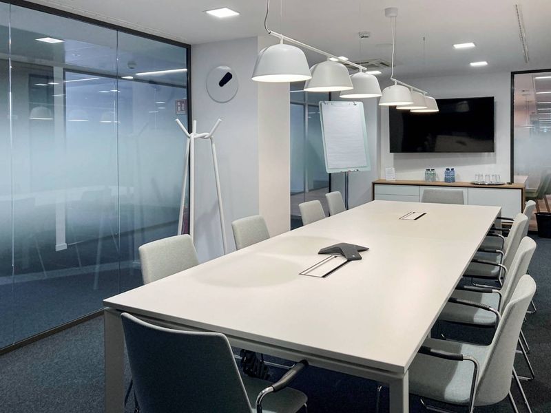 Modern professional boardroom featuring glass partition walls, integrated pendant lighting, and built-in storage cabinetry in a clean, contemporary office environment.