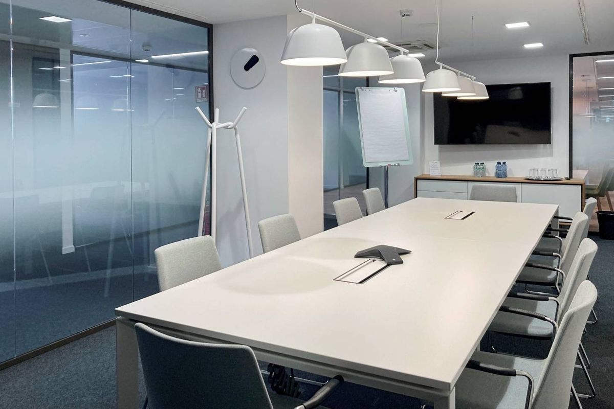 Modern professional boardroom featuring glass partition walls, integrated pendant lighting, and built-in storage cabinetry in a clean, contemporary office environment.