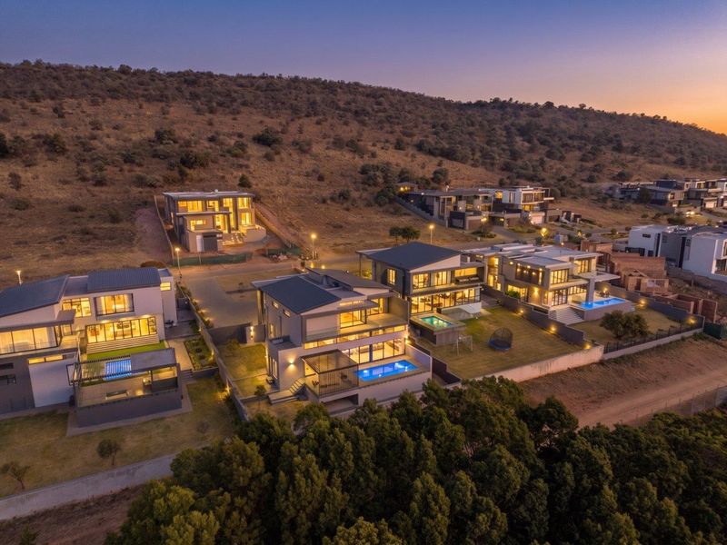 An aerial view of a modern residential estate featuring multiple contemporary homes with private swimming pools, landscaped gardens, and scenic hillside surroundings at dusk.