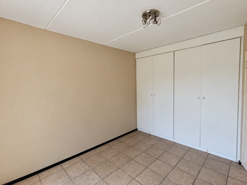An empty bedroom featuring neutral wall paint, tiled flooring, and built-in white cupboards providing ample storage space.
