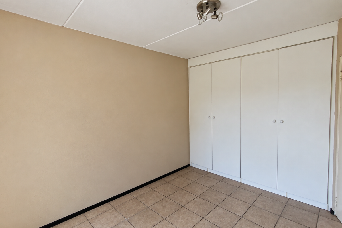 An empty bedroom featuring neutral wall paint, tiled flooring, and built-in white cupboards providing ample storage space.