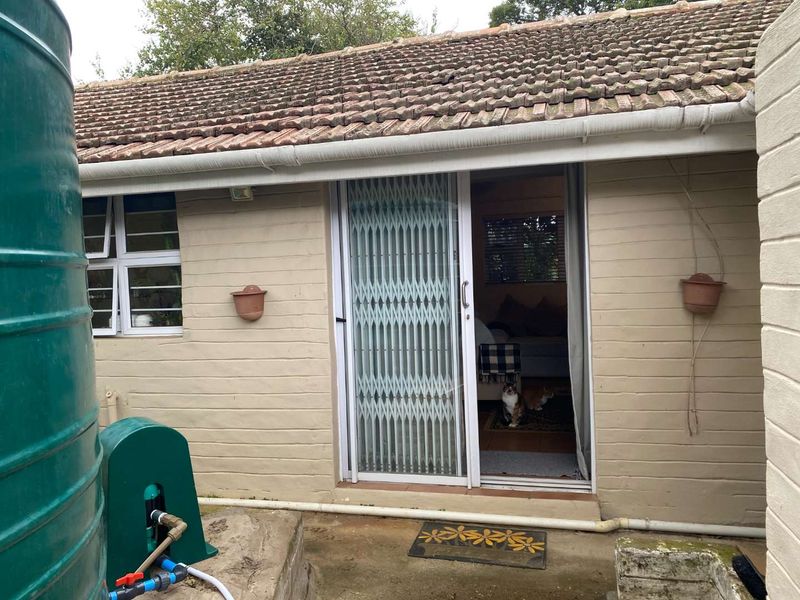 Rear exterior view of the cottage featuring a tiled roof, sliding glass door with security gate, and an external water tank installation.