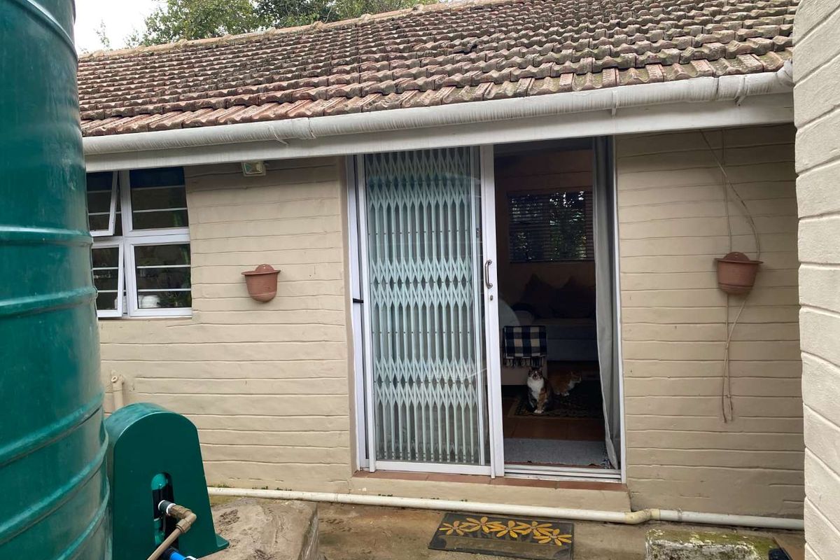 Rear exterior view of the cottage featuring a tiled roof, sliding glass door with security gate, and an external water tank installation.