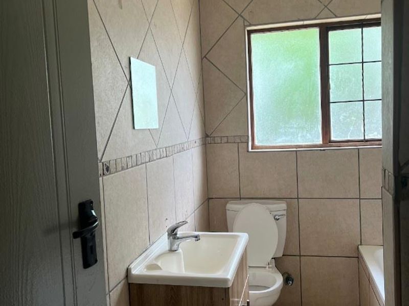 A functional bathroom featuring a vanity cabinet with basin, toilet, and bathtub, finished with tiled walls and flooring.