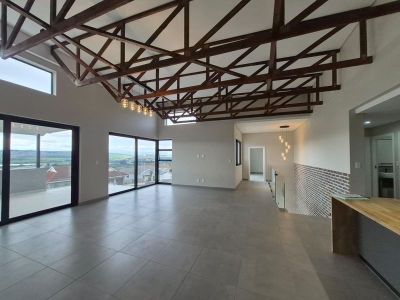 Spacious open-plan living area featuring high exposed timber trusses, large sliding doors with scenic views, and modern tiled flooring.