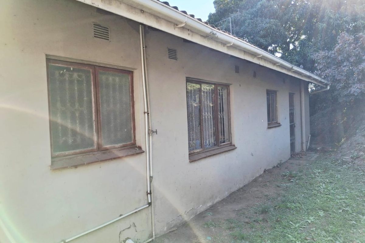 Rear exterior view of the house showing weathered plaster walls, security bars on windows, and functional guttering system.