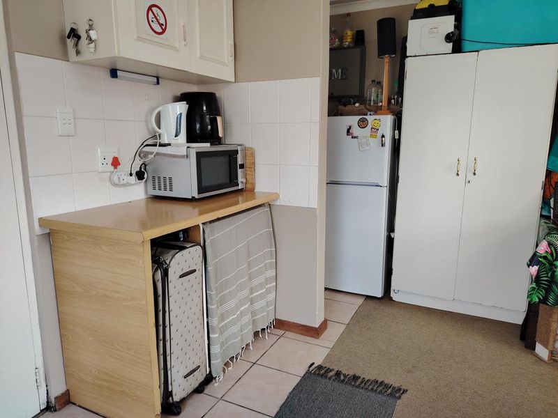 A compact kitchen area featuring tiled splashbacks, laminate countertops, and built-in cabinetry, currently used as a functional utility and storage space.