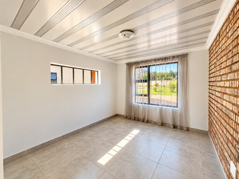 A bright, empty living room featuring tiled floors, an exposed brick feature wall, and large windows with garden views.