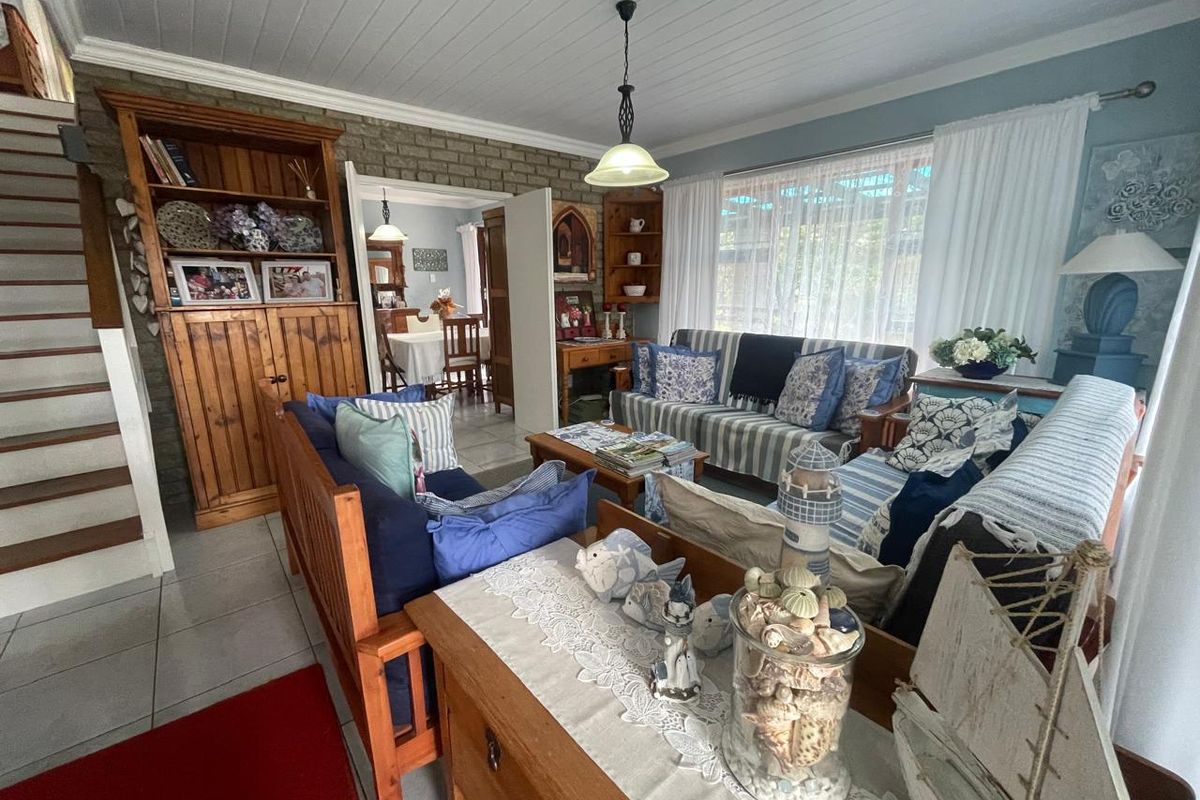 A cozy living room featuring a brick feature wall, timber staircase, tiled flooring, and a tongue-and-groove ceiling, with an open flow to the dining area.