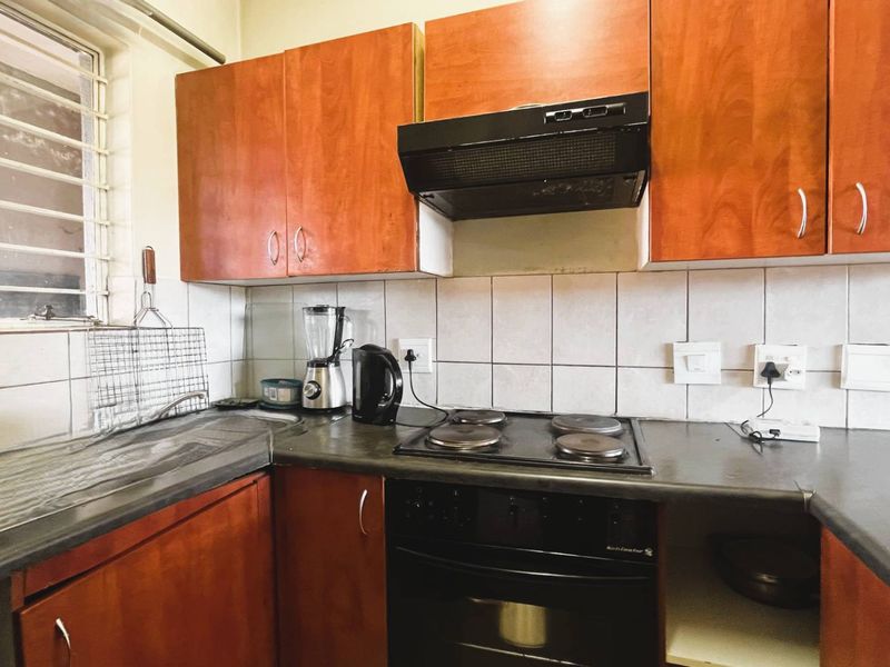 A functional kitchen featuring wood-look cabinetry, a dark laminate countertop, built-in oven and hob, and a tiled backsplash with a window for natural light.