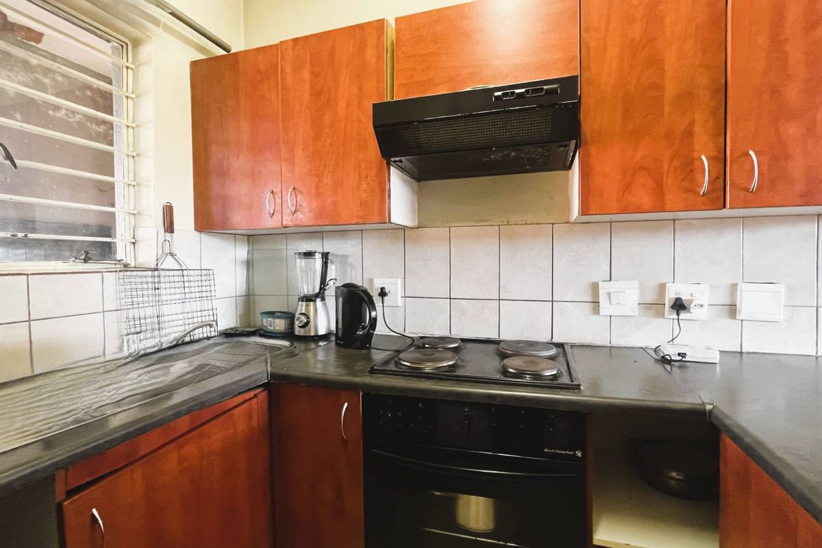 A functional kitchen featuring wood-look cabinetry, a dark laminate countertop, built-in oven and hob, and a tiled backsplash with a window for natural light.
