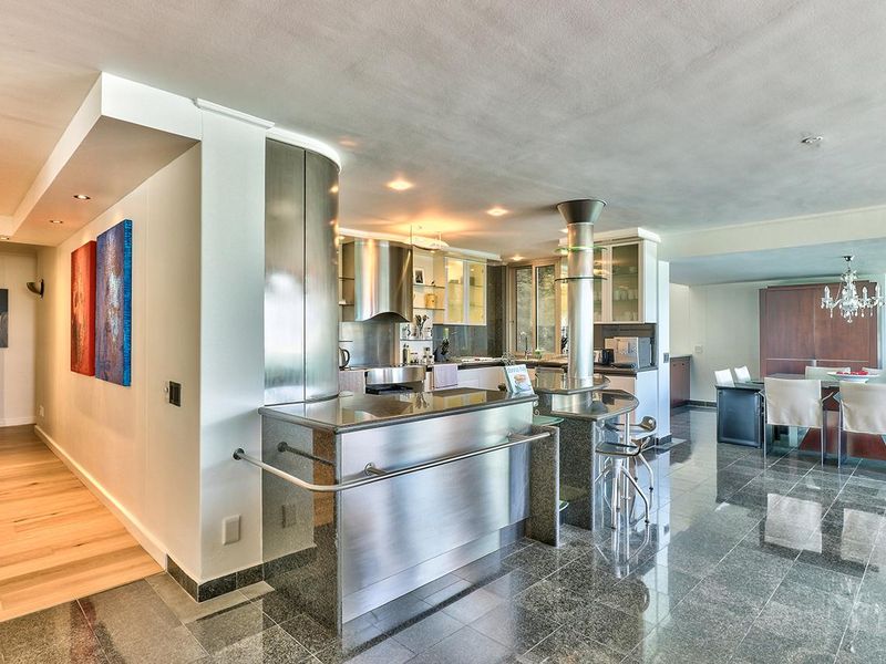 Spacious open-plan kitchen and dining area featuring modern stainless steel cabinetry, granite flooring, and integrated lighting, creating a sleek and functional living space.