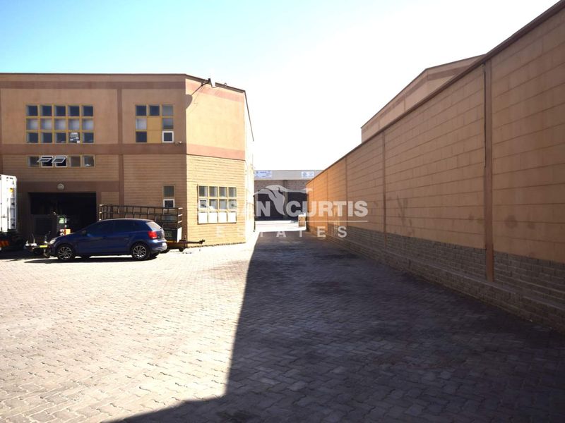 Industrial property exterior featuring a paved yard area, masonry boundary wall, and multi-pane windows on the building facade.