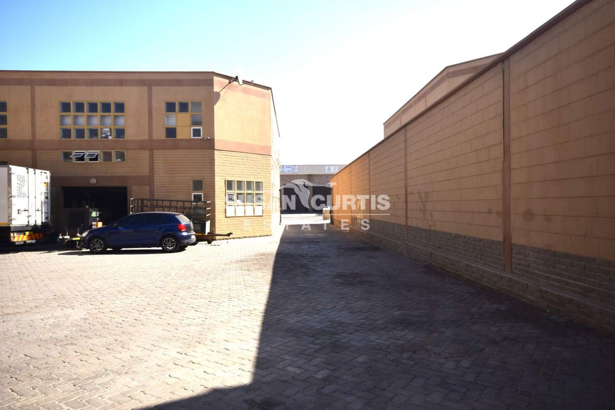 Industrial property exterior featuring a paved yard area, masonry boundary wall, and multi-pane windows on the building facade.