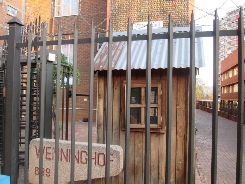 Front entrance view of the apartment complex featuring security fencing with razor wire and a small timber guard hut.