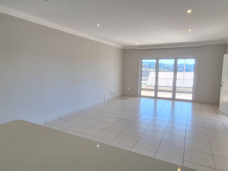 Spacious open-plan living area featuring neutral tiled flooring, recessed lighting, and large sliding glass doors leading to an outdoor balcony.