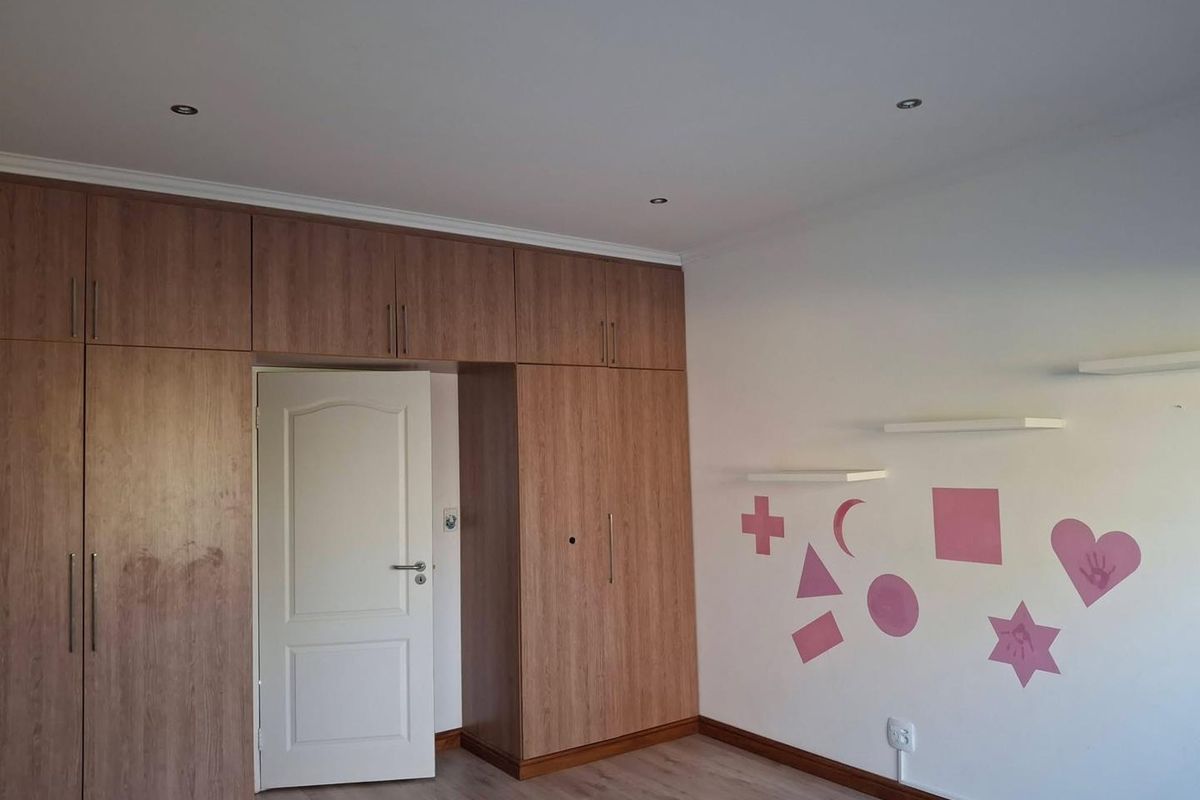 A clean, empty bedroom featuring extensive built-in wooden cabinetry, laminate flooring, recessed lighting, and decorative wall shelving.