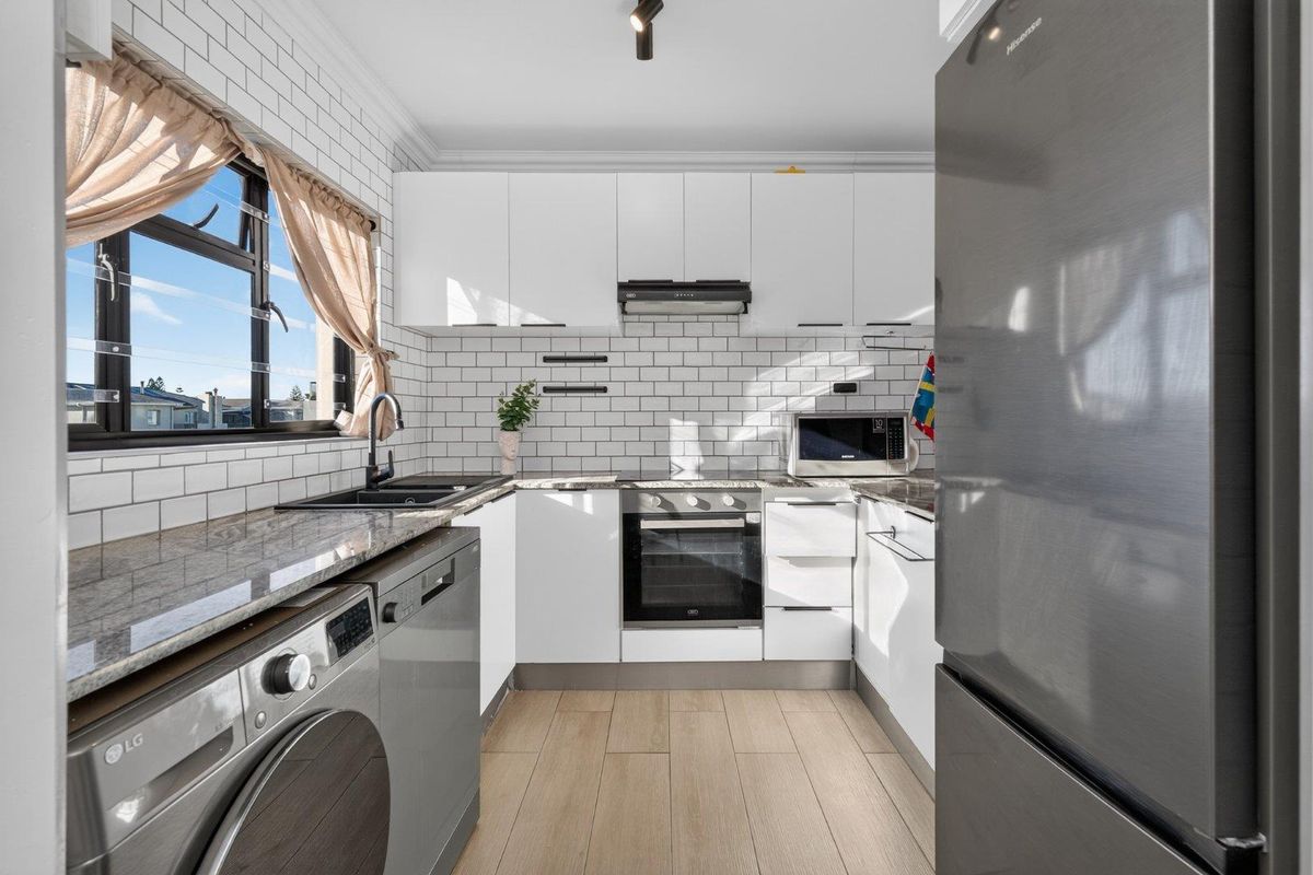 Modern kitchen featuring white cabinetry, subway tile backsplash, granite countertops, integrated oven, extractor fan, and wood-look flooring.