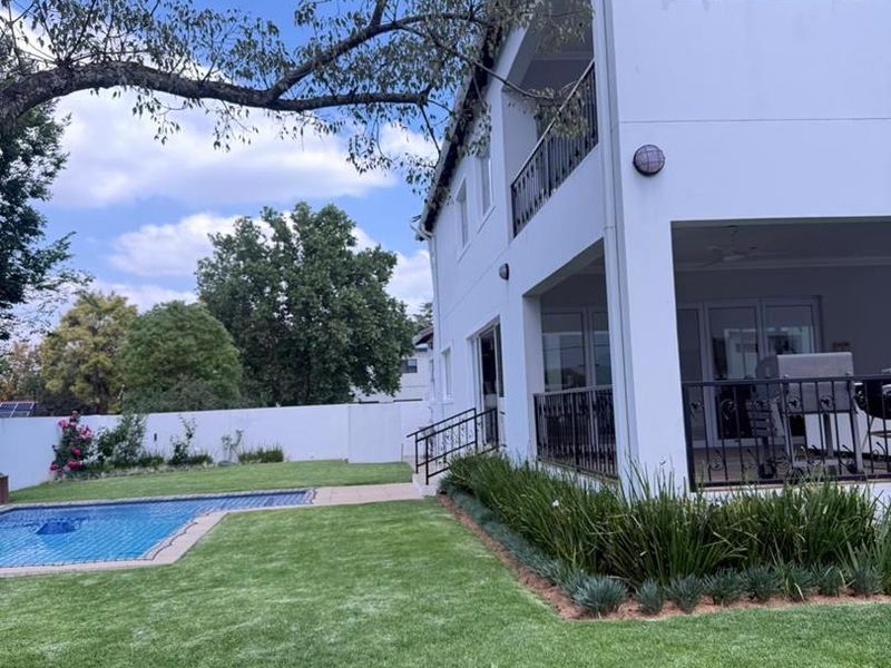 Rear view of the property featuring a swimming pool, landscaped garden, and a multi-level covered patio and balcony with wrought iron railings.