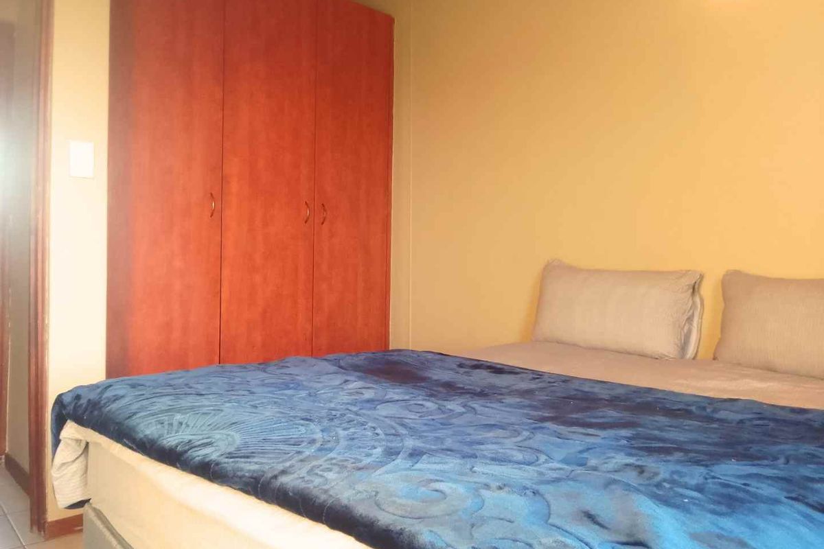 A bedroom featuring built-in wooden cupboards and tiled flooring.
