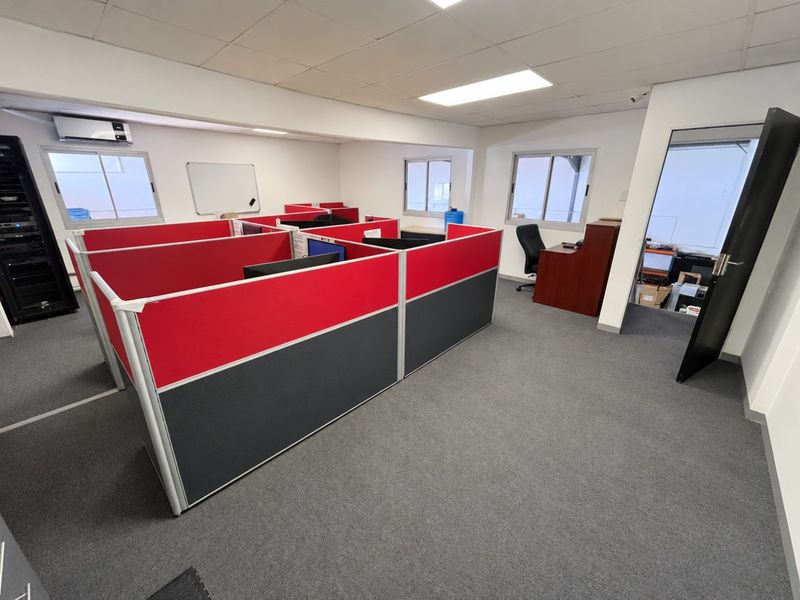 A functional office space featuring partitioned cubicles, carpeted flooring, recessed lighting, and a dedicated server rack area.