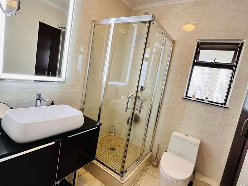 Modern bathroom featuring a glass shower enclosure, sleek black vanity with a vessel sink, back-to-wall toilet, and an elegant LED backlit mirror.