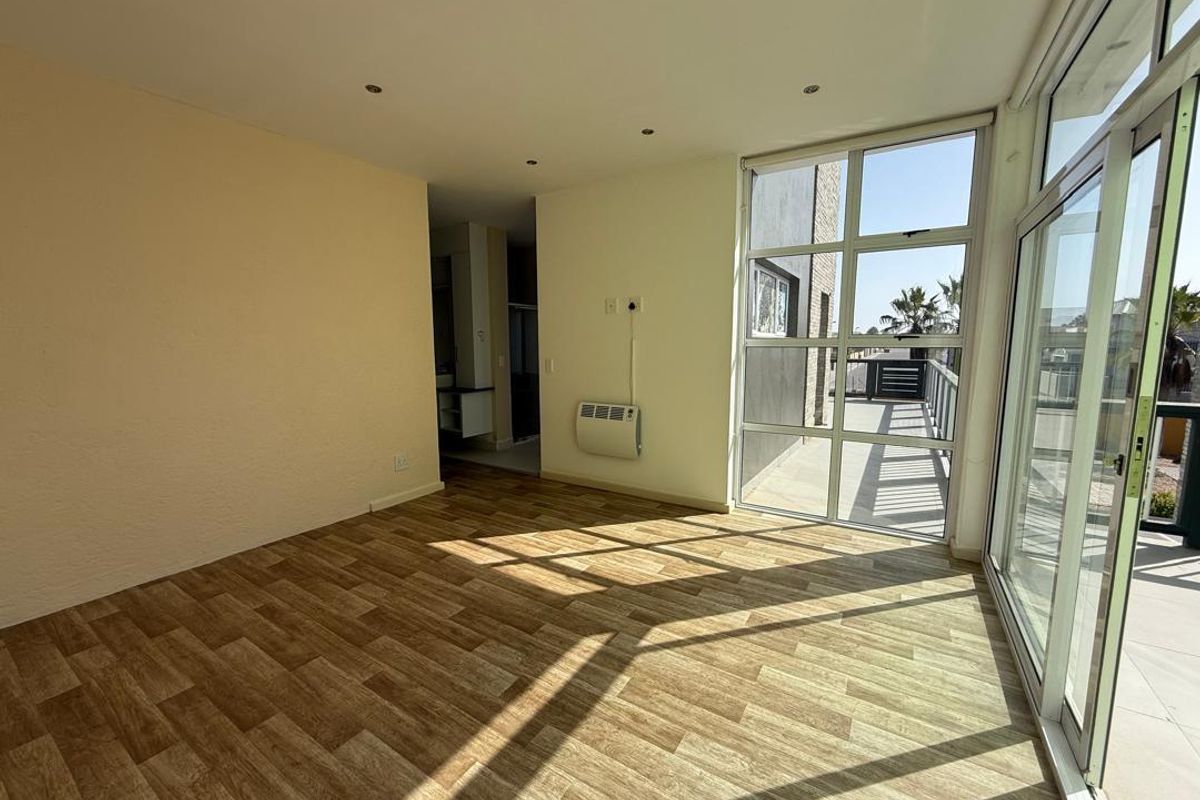 Bright living area featuring wood-look flooring, recessed ceiling lighting, a wall-mounted air conditioning unit, and large floor-to-ceiling windows leading to an outdoor balcony.