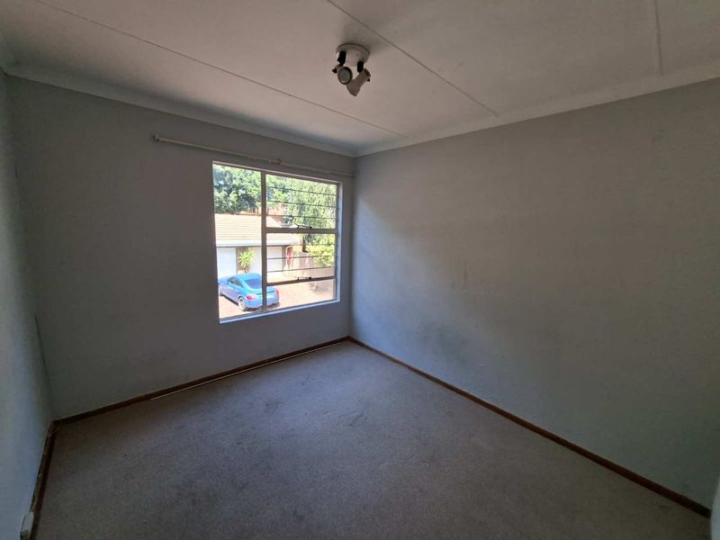 An empty bedroom featuring neutral walls, carpet flooring, and a window providing natural light.
