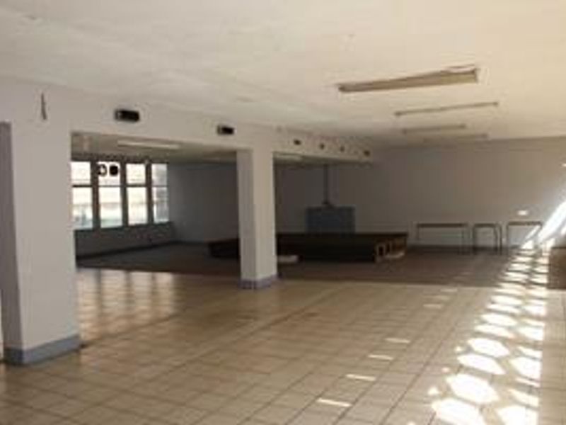 A large, open-plan commercial space featuring tiled flooring, structural columns, and ample natural light from large windows, suitable for various business configurations.