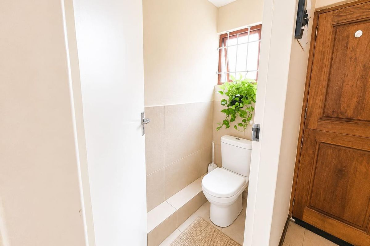 A compact, well-maintained guest bathroom featuring neutral wall tiles, a modern toilet, and a window with security bars.