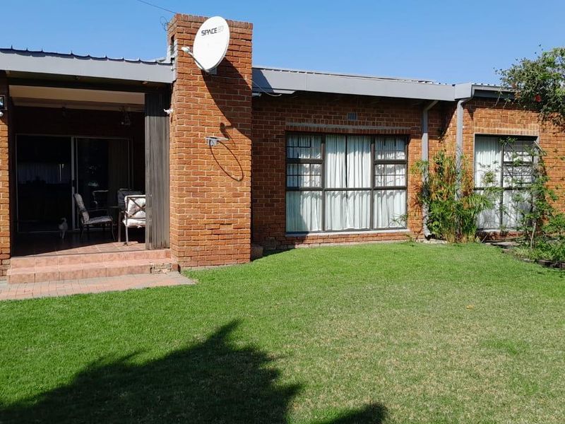 Rear view of a brick house featuring a covered patio area, large sliding glass doors, and a well-maintained lawn.