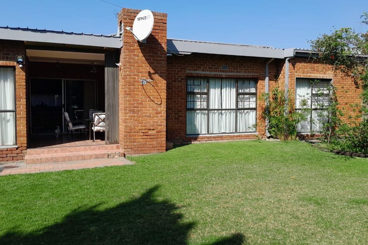 Rear view of a brick house featuring a covered patio area, large sliding glass doors, and a well-maintained lawn.