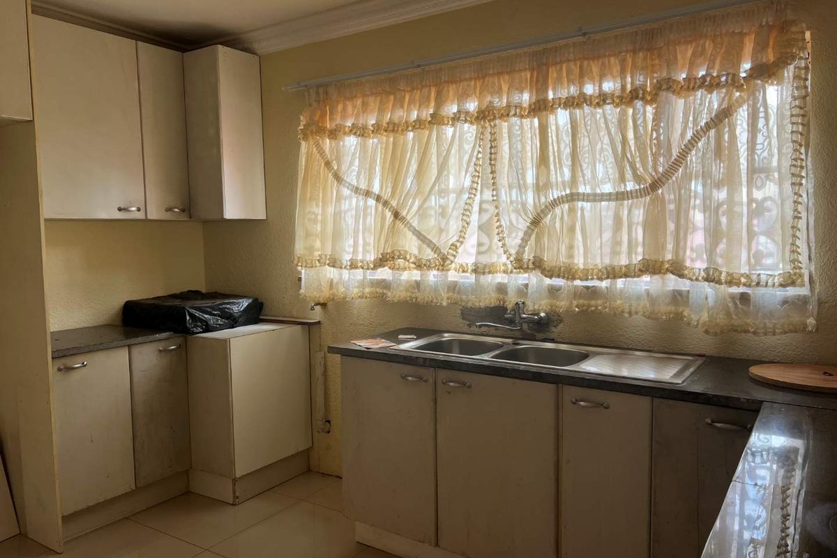 A dated kitchen featuring original cabinetry, a double-basin stainless steel sink, and tiled flooring, offering potential for modernization and renovation.