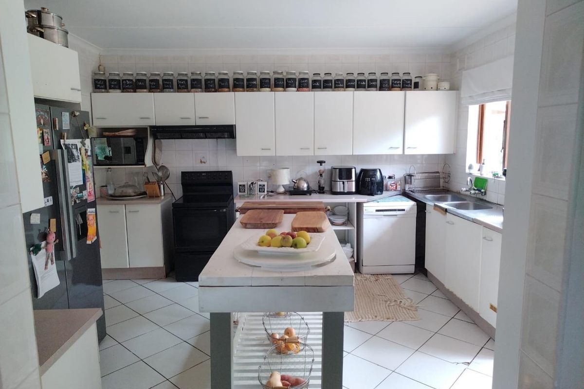 A functional kitchen featuring white cabinetry, tiled splashbacks, tiled flooring, and a central island, providing ample storage and workspace for daily meal preparation.