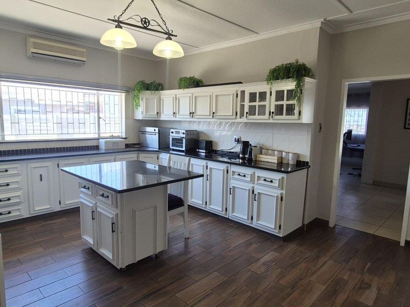 A well-maintained kitchen featuring white cabinetry, dark stone countertops, a central island, and wood-look tiled flooring with integrated air conditioning.