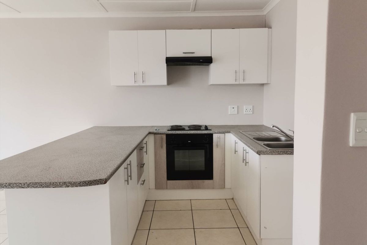 A clean, modern kitchen featuring white cabinetry, stone-look countertops, integrated electric oven and hob, and tiled flooring in an open-plan layout.