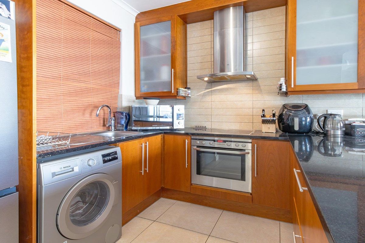 A functional kitchen featuring wood-finish cabinetry, granite countertops, a built-in oven with extractor fan, and integrated laundry plumbing.