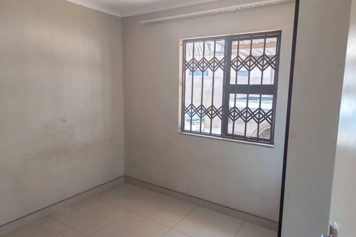 An empty bedroom featuring tiled flooring and a window fitted with a security gate.